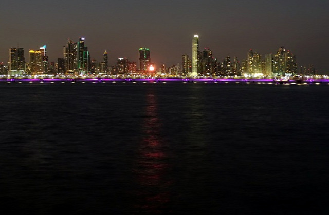 Éjszakai látkép a felhőkarcolók előtt futó, oceánba épített autópályával
